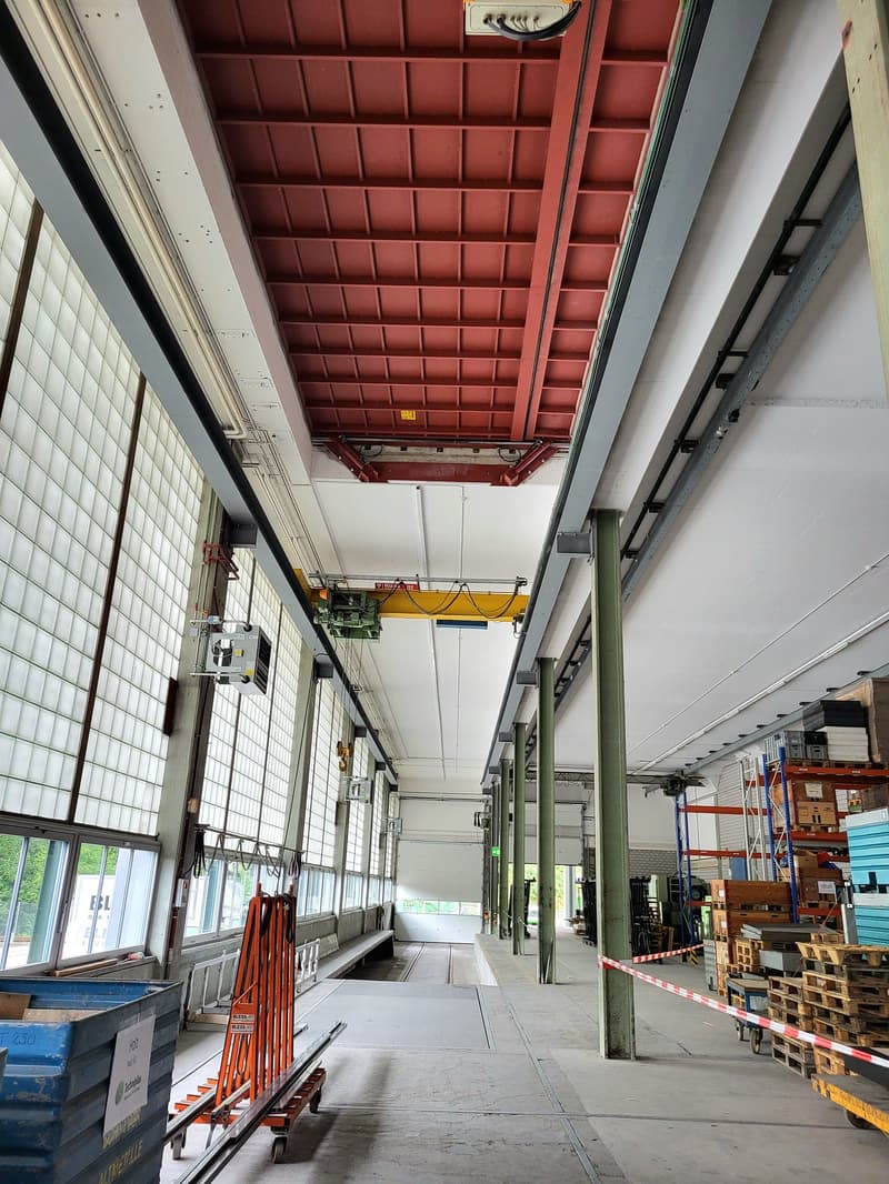 Large industrial warehouse space with high ceilings, red metal beams, and storage racks and equipment visible.