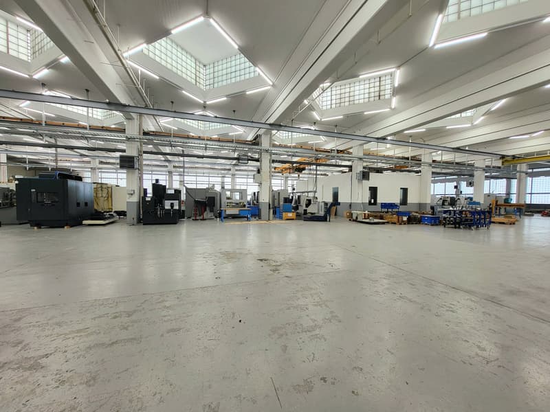 Large industrial workshop space with high ceilings, concrete floors, and various machinery and equipment such as CNC machines and tool chests. The space appears to be well-lit with overhead lighting.