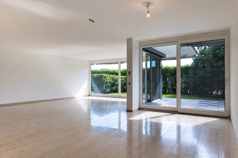 Empty room with light-colored tiled flooring, white walls, large sliding glass doors leading to an outdoor area, and natural light streaming in.