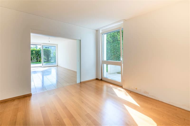 Empty room with light wooden flooring, white walls, and large sliding glass doors leading to an outdoor area.