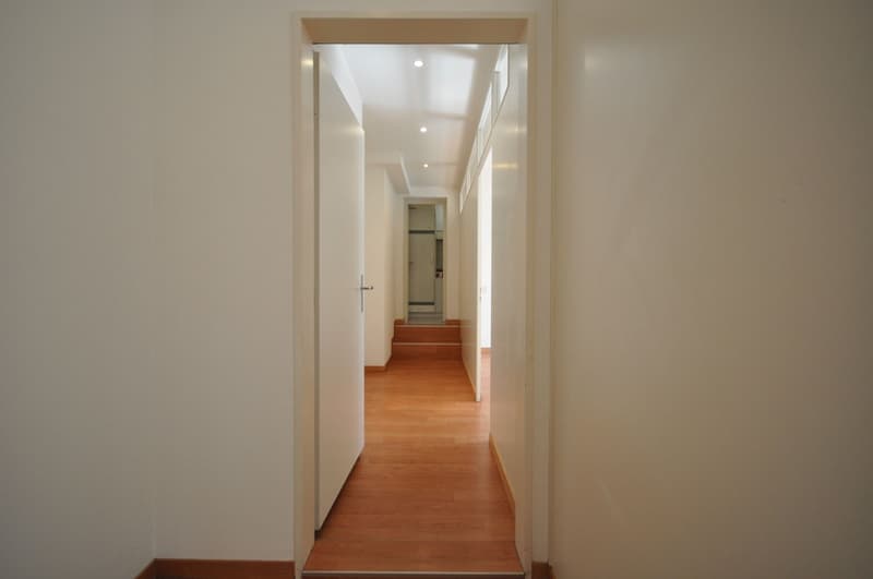Empty hallway with wooden floor, white walls, open door, and staircase