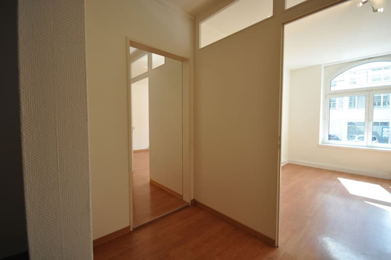 Empty room with wooden floor, white walls, large window, mirror on the door