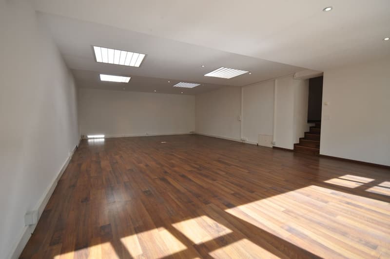Empty room with wooden floor, white walls, and ceiling lights