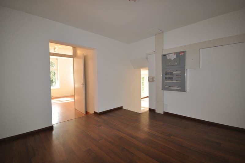 Empty room with wooden floor, white walls, open door, and electrical panel on the wall.