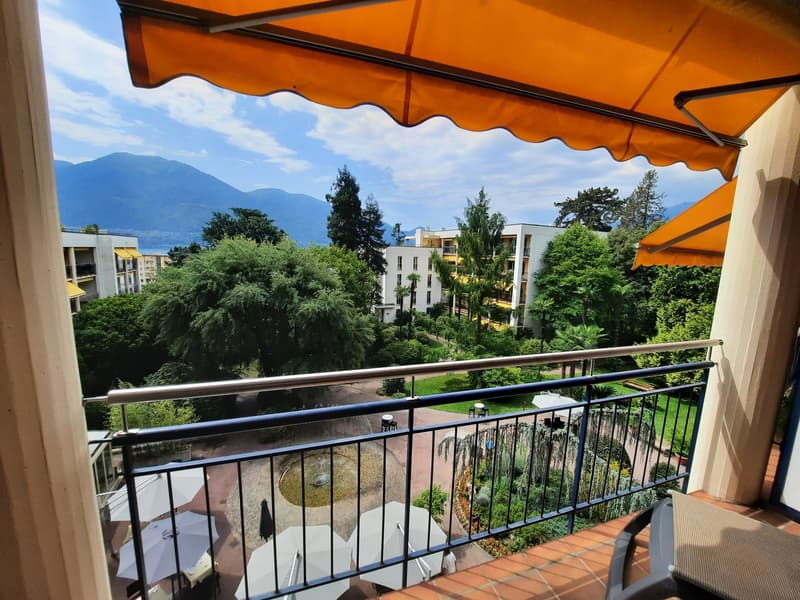 orange awning, metal railing, umbrellas, plants, mountains, trees, buildings, fountain, people walking