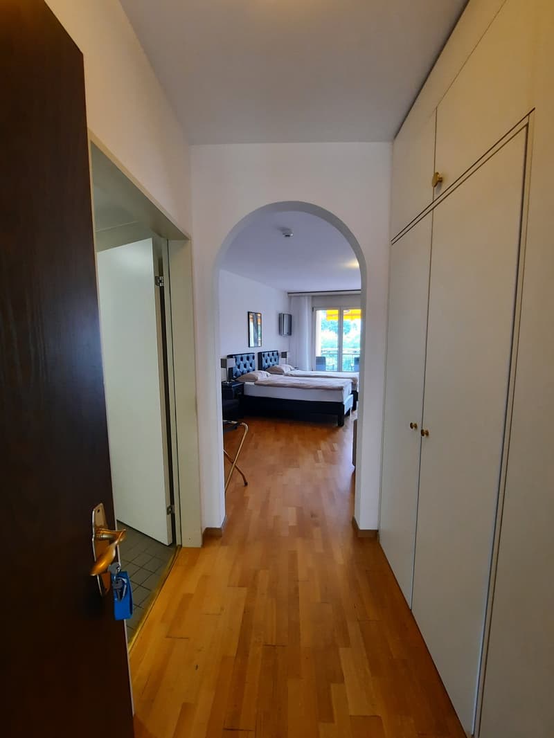 Open hallway with wooden floor, two beds with pillows, closets, lamps, balcony