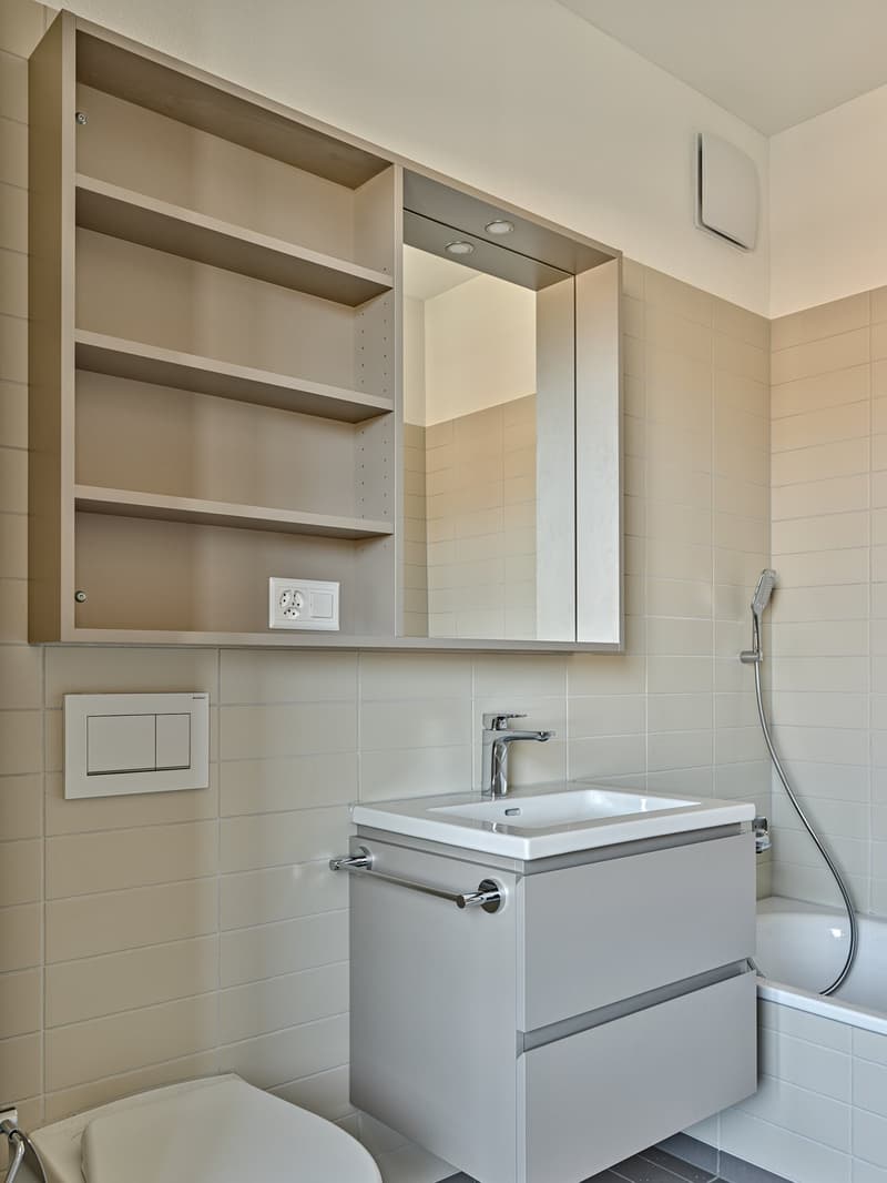 Bathroom with white tile walls, vanity with sink, mirror cabinet, and shelving above the toilet