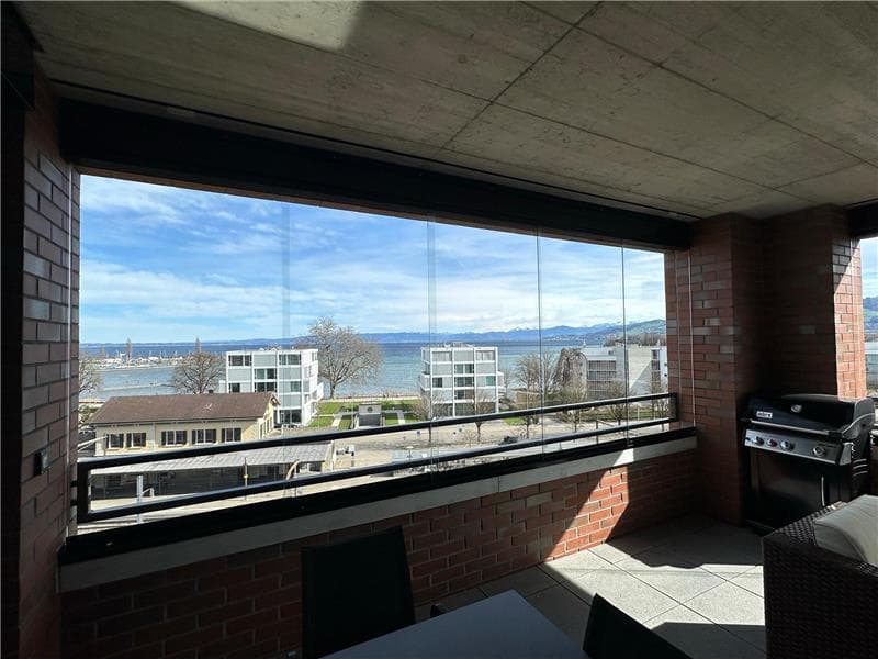 Spacious apartment with large windows offering a panoramic view of the surrounding buildings and the water in the distance. The apartment has a balcony or terrace accessible from the living area.