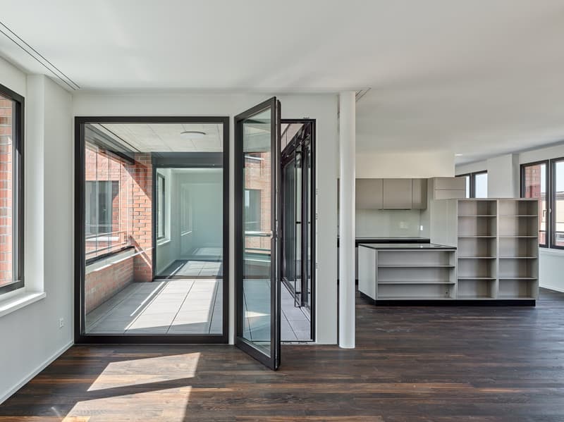 open double door to a balcony, large windows, modern minimalistic style, wooden floor, kitchen with cabinets and shelves, brick walls