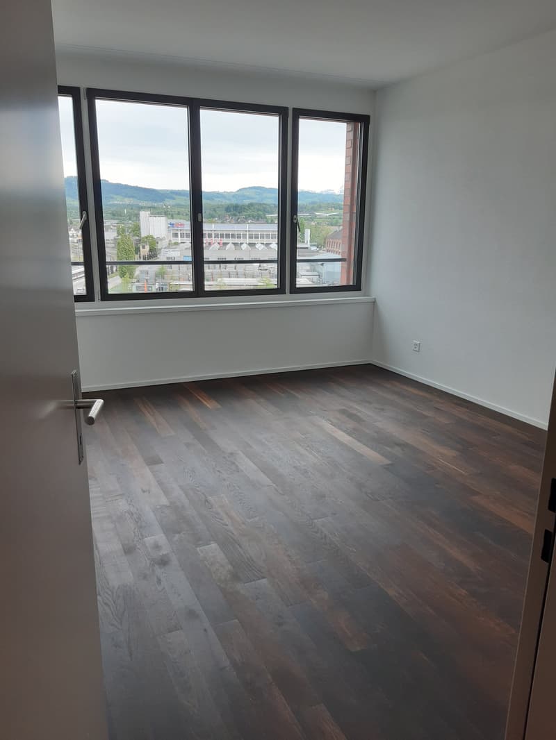 large empty room with wooden floors and windows overlooking the city