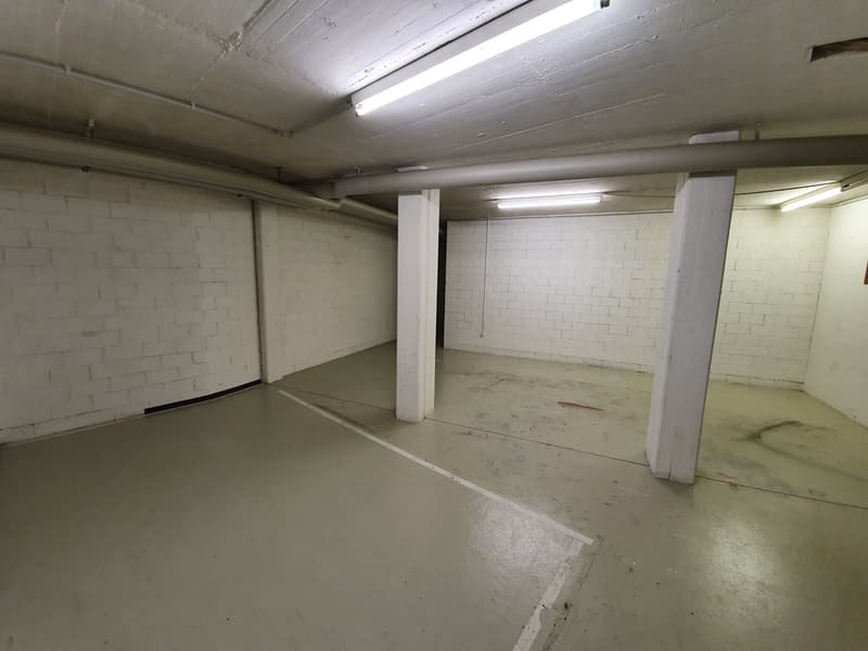 Empty parking space with white walls, concrete floor, and ceiling lights