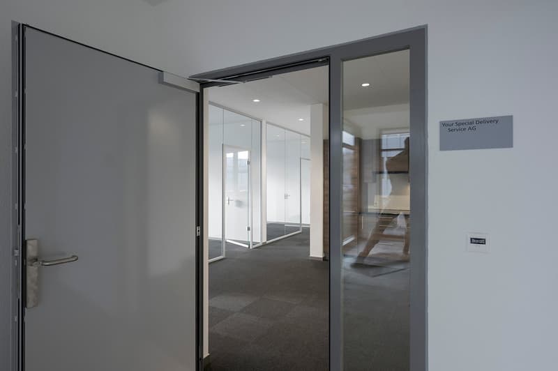 An open door with gray frame, glass wall behind the door, and text sign on the right wall.
