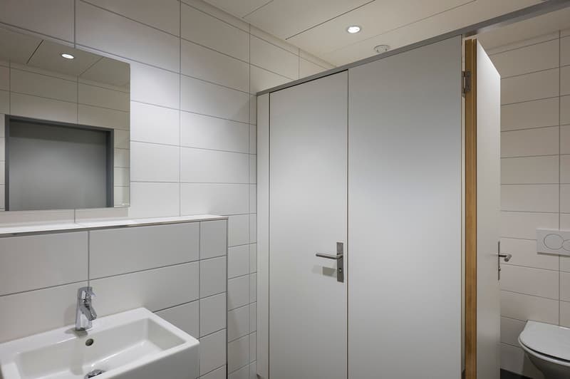 Clean bathroom with white tiled walls, sink, toilet, and mirror. The lighting is ceiling-mounted.