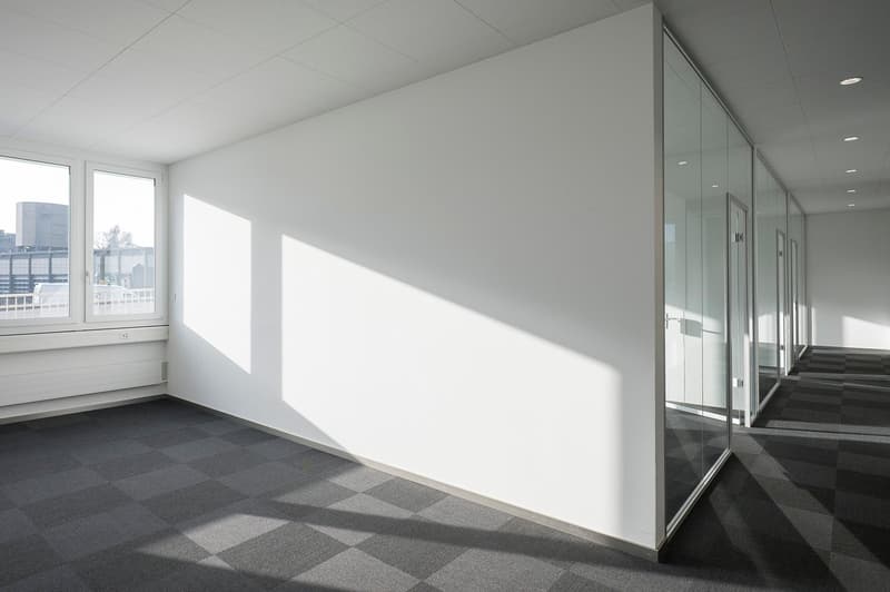 Empty office with white walls, glass doors, and windows, checkerboard patterned flooring, ceiling lights