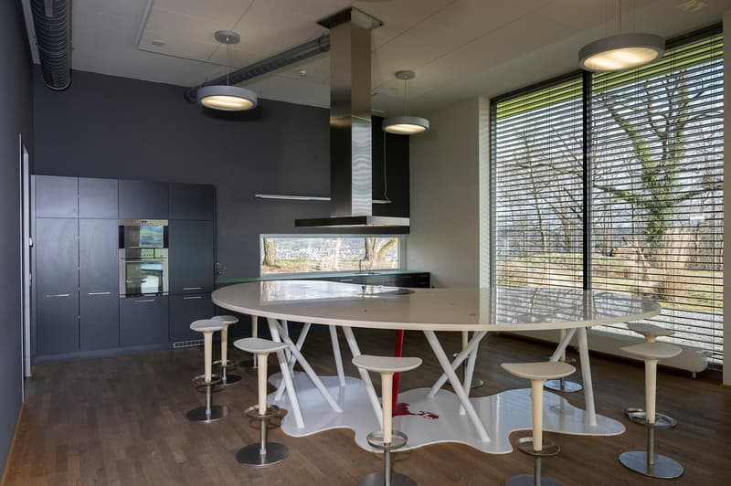Modern kitchen with dark gray cabinets, round dining table with white chairs, large windows overlooking outdoor scenery