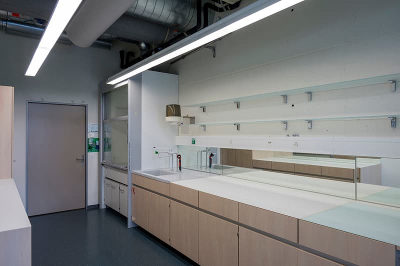 Modern, open kitchen with white countertops, wooden cabinets, and a dishwasher. The kitchen has ample counter space and storage. The room is well-lit with overhead lighting and large windows.