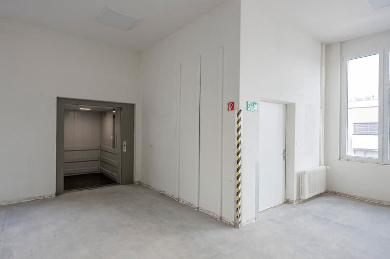 empty room, cement floor, elevator entrance, white walls, white door, white radiator, window, security signs