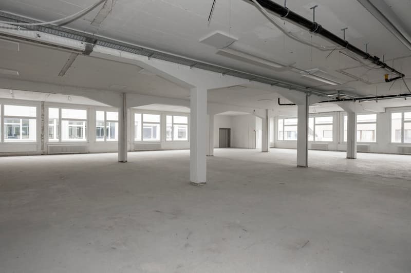 Open warehouse space, concrete floor, exposed beams, large windows, industrial aesthetic