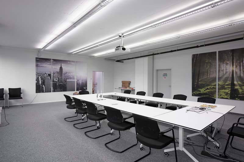 Conference room with long tables, black chairs, projector, white walls, two large images on wall, white carpet