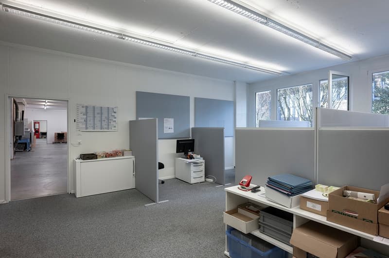 Office room, gray office partitions, white shelves, black and white office chairs, multiple boxes, monitor, storage boxes, open door, windows, office furniture