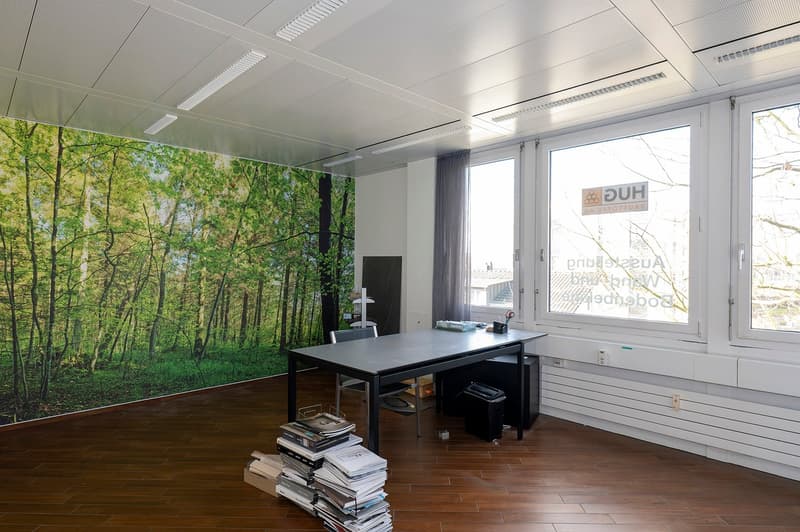 empty room, wooden flooring, large window, desk with stacked magazines, green wall wallpaper, chair, computer