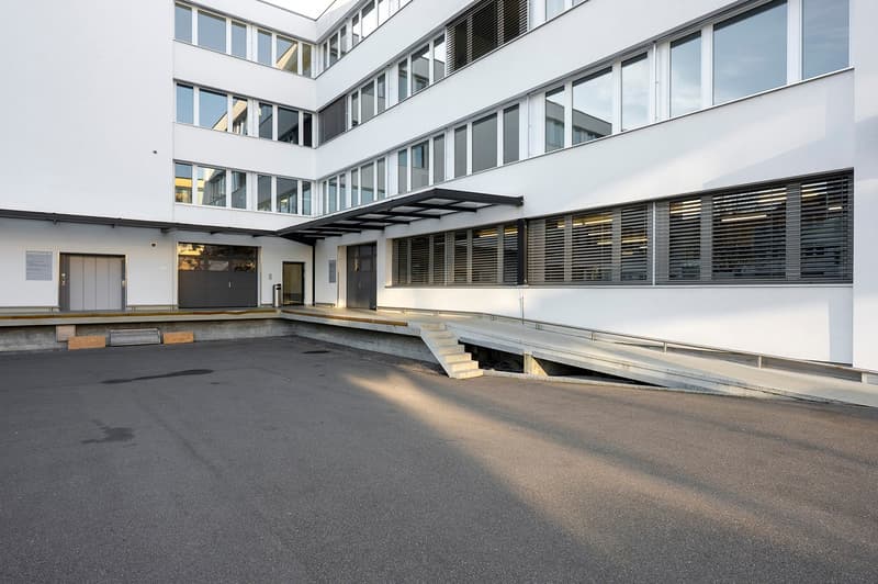 white exterior, multiple windows, accessible ramp, concrete parking lot, double doors