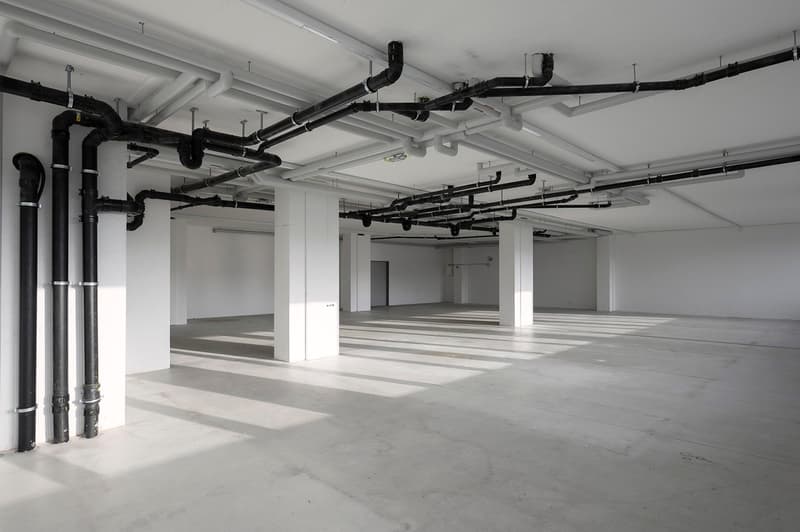 Empty room, white walls, concrete floor, metal pipes on ceiling and wall
