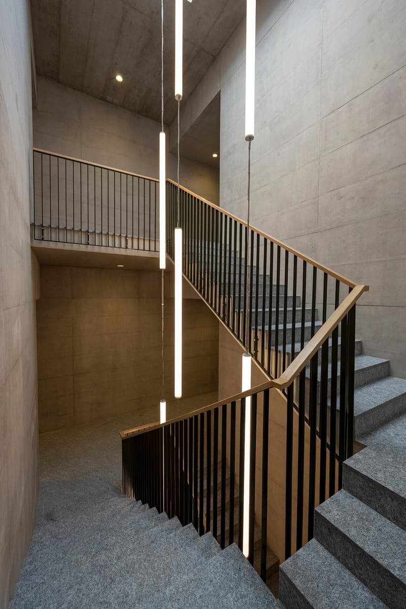 Modern architecture, staircase, grey carpeted steps, black metal railings, three vertical lights, white tiled walls