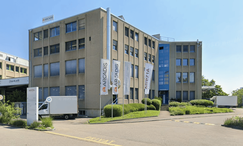 3 story building, glass windows, signboards, greenery in front, white truck parked