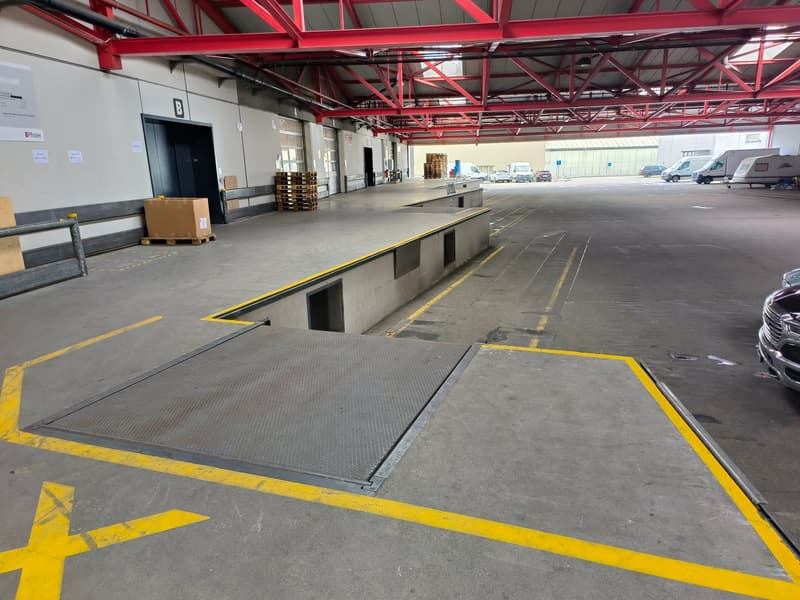 large warehouse, concrete floor, yellow markings, metal ramps, storage boxes, vehicles parked