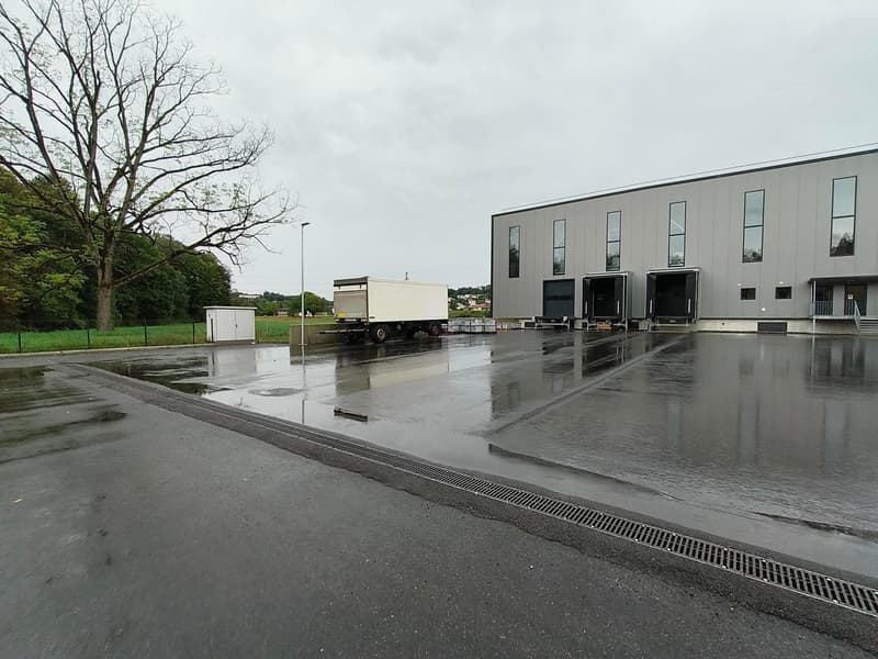Industrial building with large parking area, truck parked, large windows, metal grates