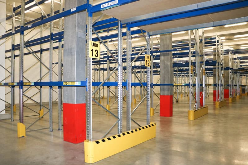 Warehouse with metal shelving units, yellow and red bumpers, and yellow and red pillars