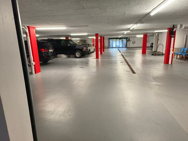 underground parking lot, red pillars, white walls, grey floor, 3 cars parked