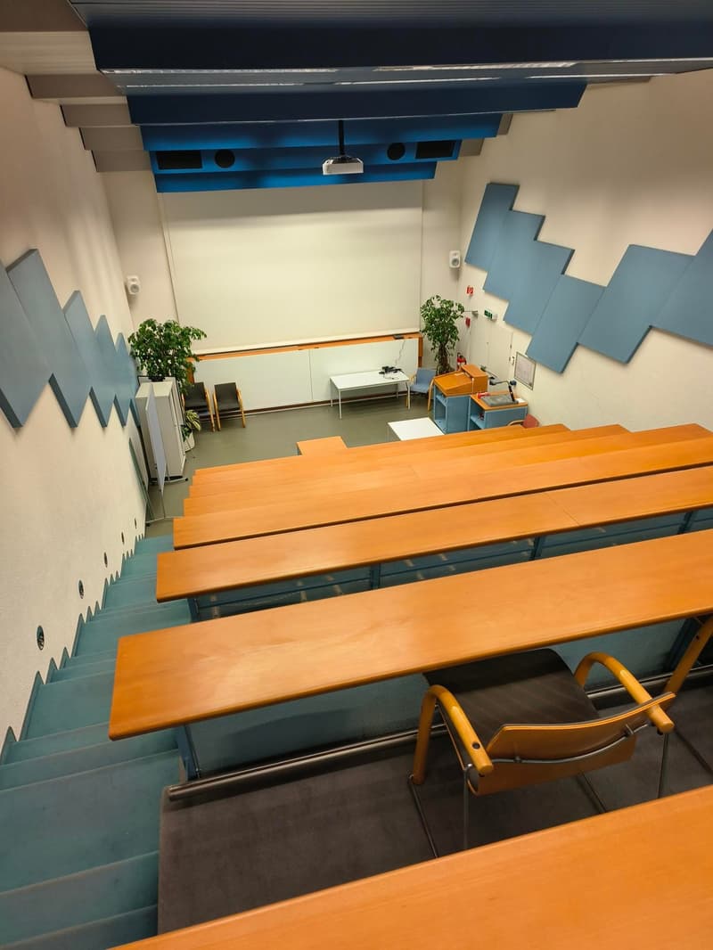 lecture hall, wooden desks, blue and white walls, stairs, plants, projector