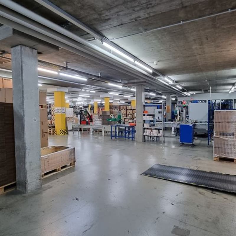 large warehouse, concrete floor, yellow pillars, fluorescent lighting, storage boxes, shelves, tables, forklift