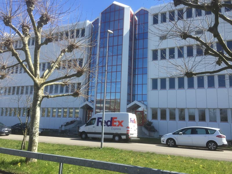 Modern office building with glass facade, multiple floors, FedEx van parked in front