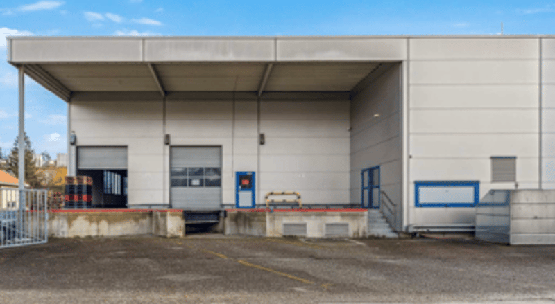 Warehouse building, white walls, two large roll-up doors, concrete floor, parking area