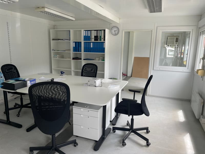 An office with a white desk, four black swivel chairs, a white bookshelf, a clock, and a white radiator.