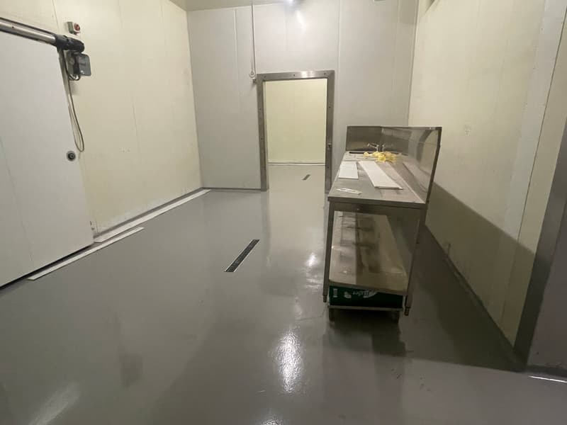 Empty room with white walls, gray floor, a stainless steel table, and a door.