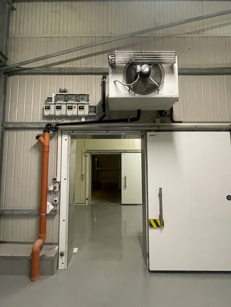 Industrial building with white walls, metal ceiling, large white door, large orange pipe, air conditioning unit, electrical panels