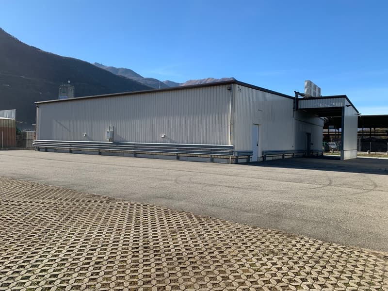 Large industrial building, white exterior, metal railings, open parking area, mountains in the background