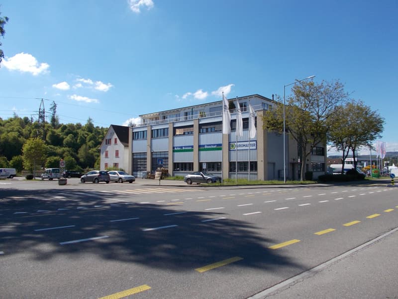 A multi-story commercial building with a modern, glass-fronted design. The building has the Euromaster logo displayed prominently, indicating it is likely a commercial or industrial facility. There are several cars parked in front of the building, and the