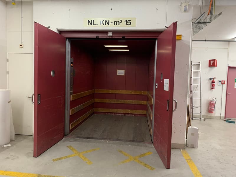 The elevator door is open, showing an interior that is red with wooden beams. The floor is gray.