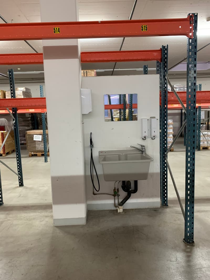 utility area with sink, soap dispenser, mirror, shelves, metal shelving, pallets, storage boxes