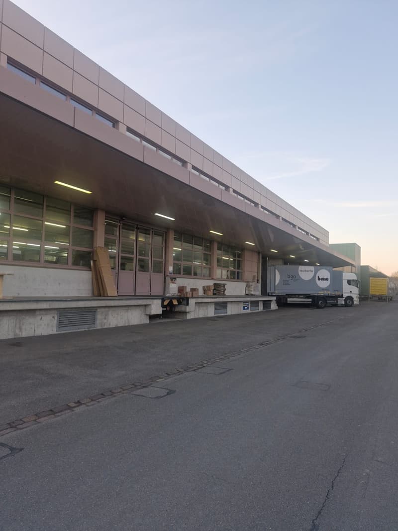 Warehouse, large windows, multiple doorways, loading bay, truck parked in front, grey concrete floor, pink panels, ventilation grates