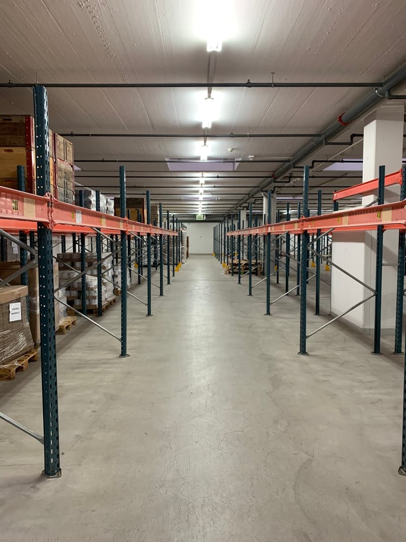 large empty warehouse, metal shelves, rows of shelving units, lights on the ceiling, empty aisles, boxes and pallets stacked