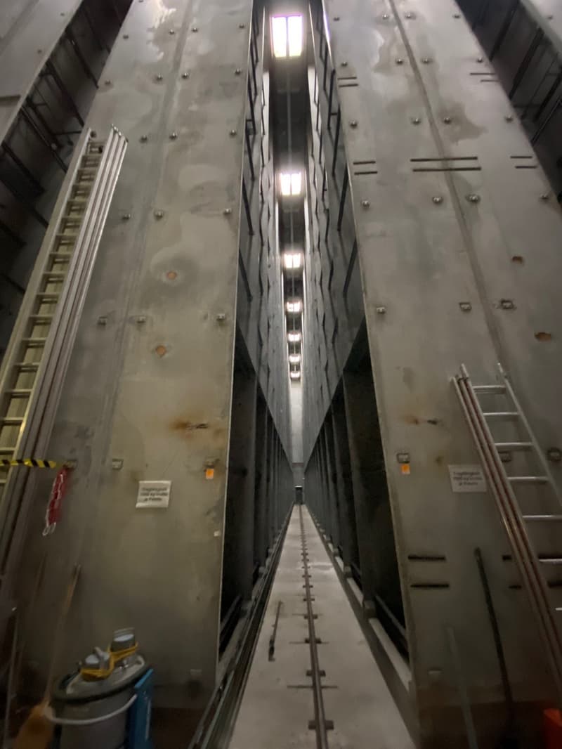 Industrial facility with metal walls, central aisle, metal ladders on both sides, white ceiling with lights, storage units on both sides.