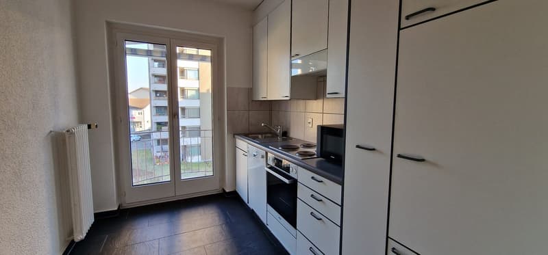 Compact kitchen with white cabinets, black countertops, and a stove. The kitchen has a sliding glass door leading to a balcony or terrace.