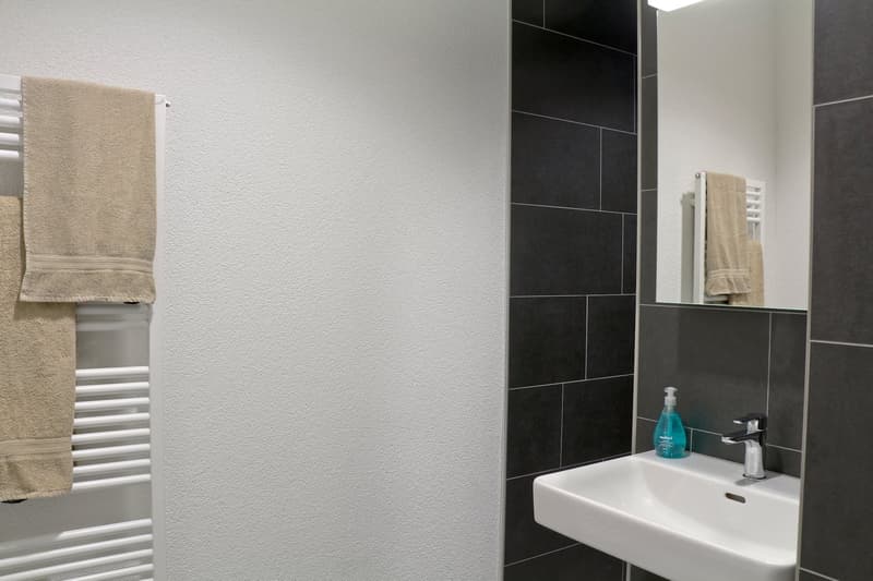 modern bathroom, white sink, black tiles, towel rack, mirror, white towel