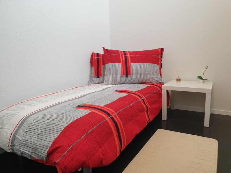 Single bed, white nightstand, red and gray bedsheets, white rug, white flowers